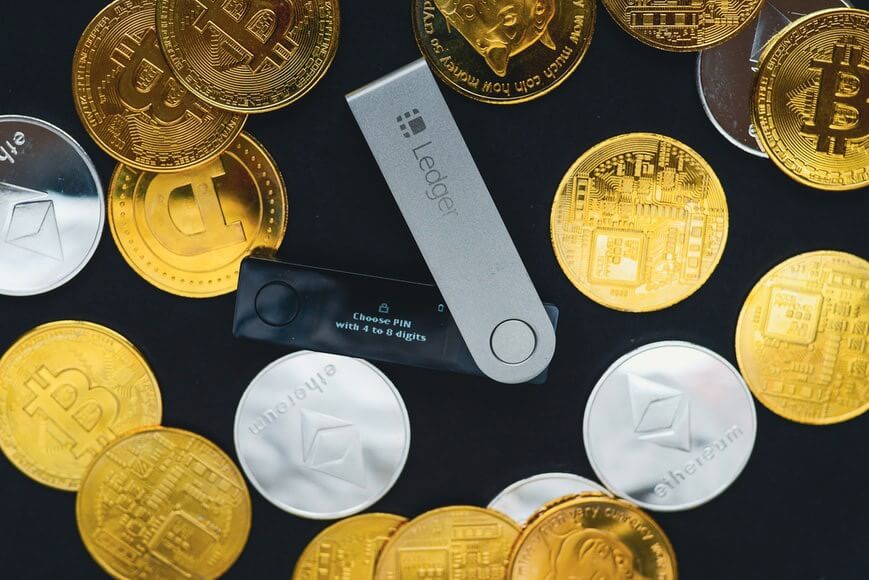 A Ledger hardware wallet surrounded with crypto coins