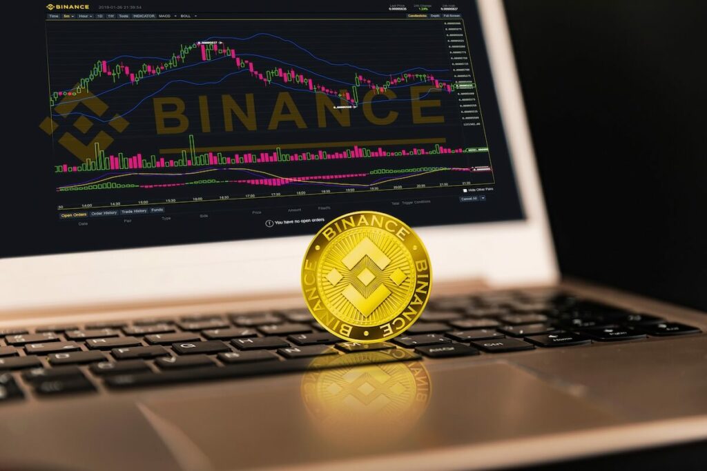 A BNB coin in front of a computer with an open Binance app